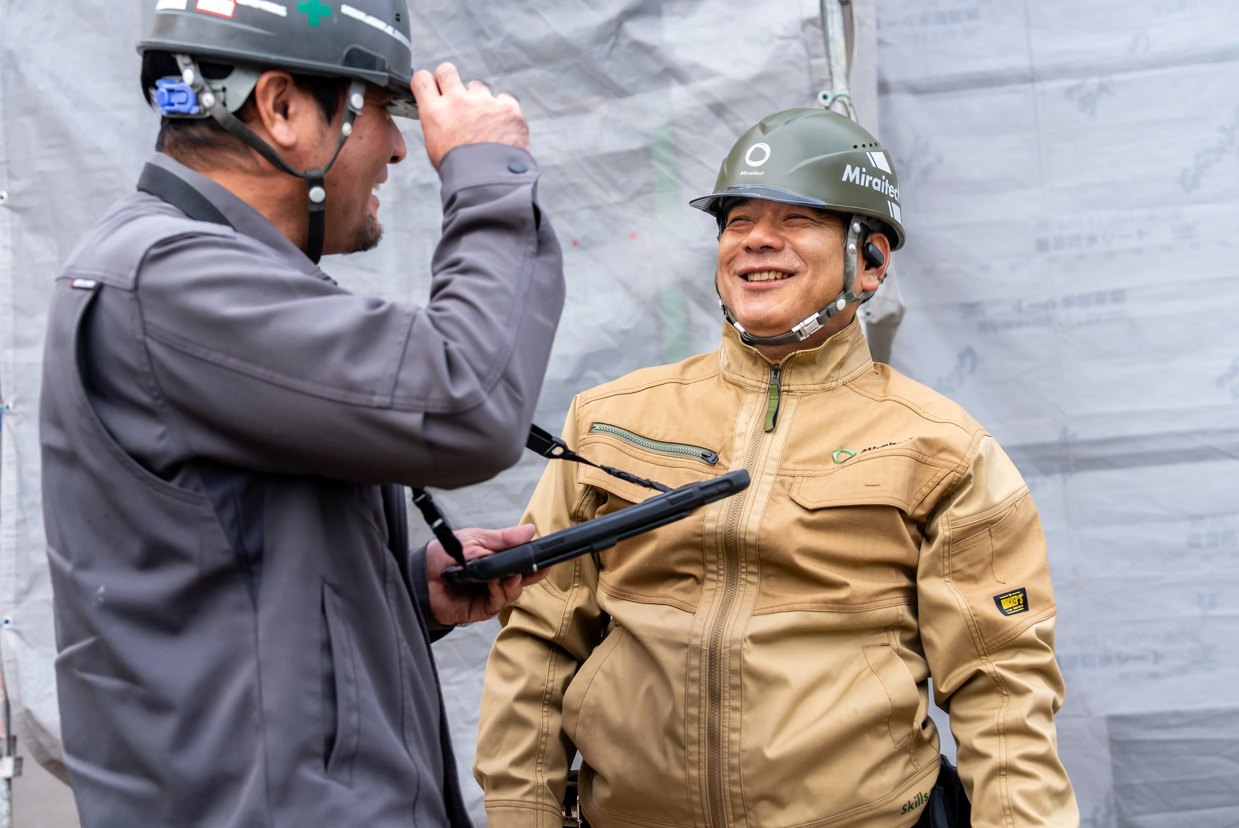 作業現場で談笑するヘルメット着用の職人二人