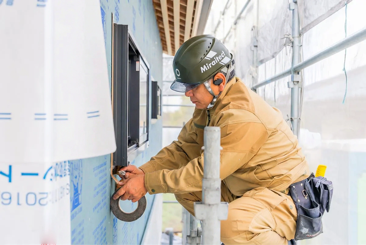 外壁下地でテープ処理を行うヘルメット着用の職人